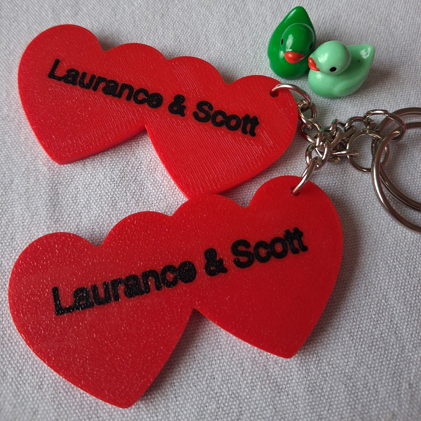 Red heart-shaped keychains with 'Laurence & Scott' branding on a gray background