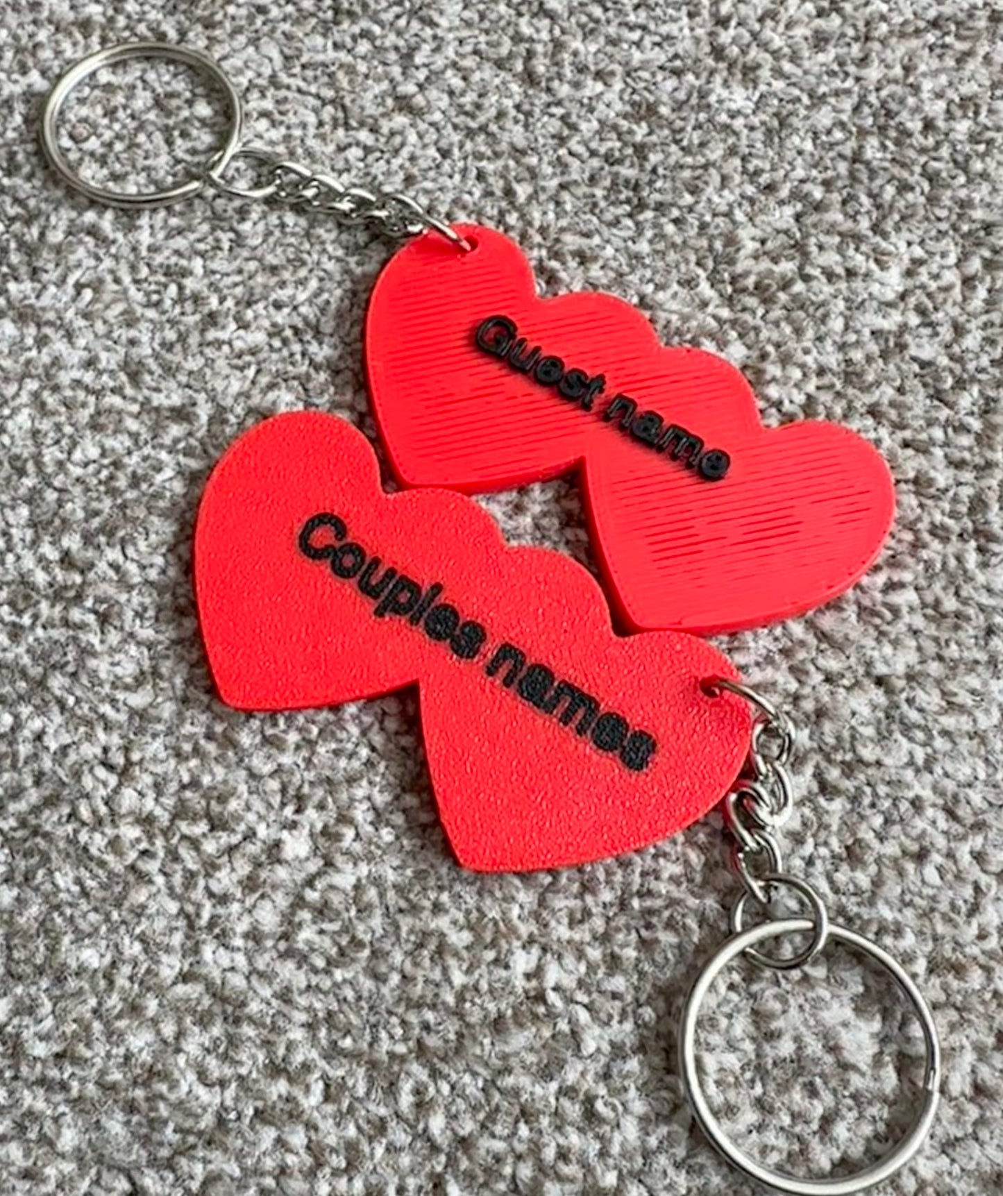 Red heart-shaped keychains with 'Couples names' text on a textured surface